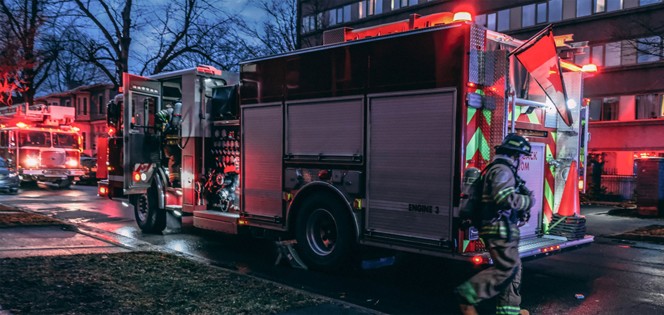 Emergency vehicles with red lights outside a residential complex at dusk.