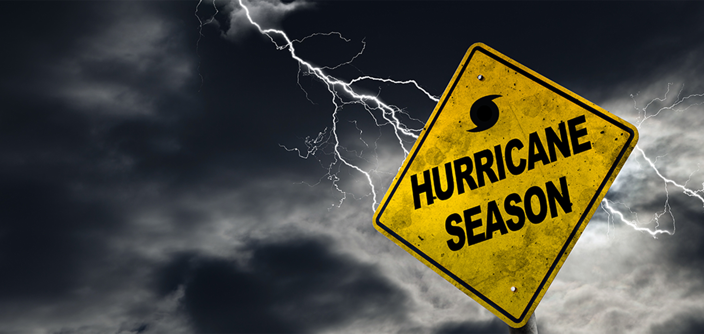 A yellow street sign reading 'Hurricane Season' with a dark stormy sky and a bolt of lightning in the background.