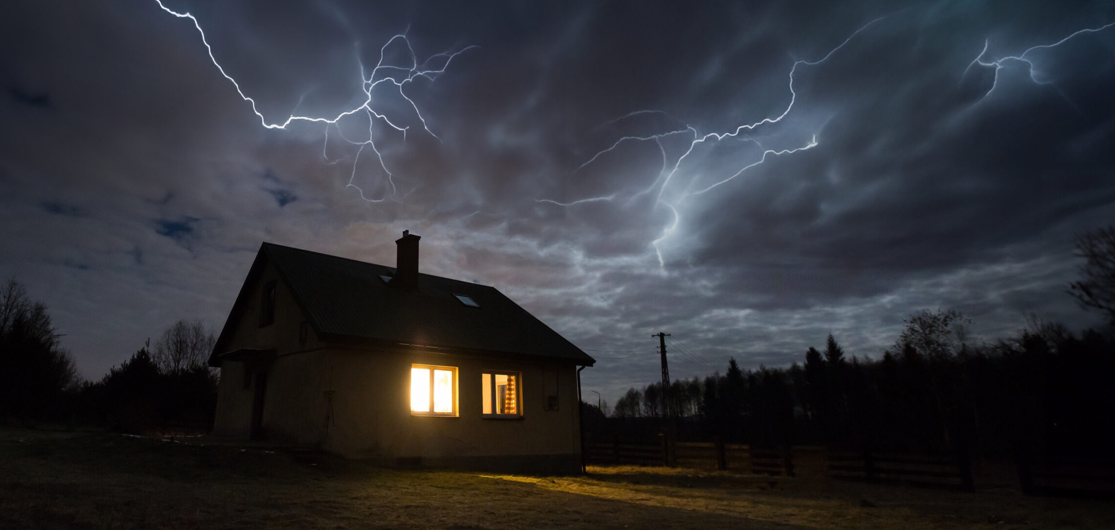 House with lights on at night during a thunder and lightning storm