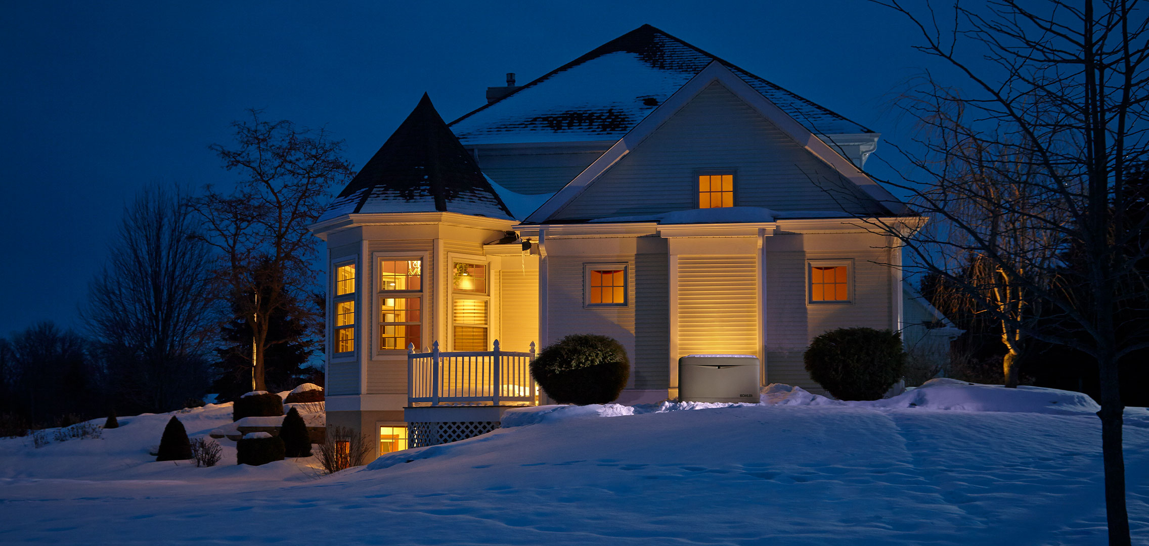 Nighttime image of residential home with interior lights on in winter with snow in yard and on roof.