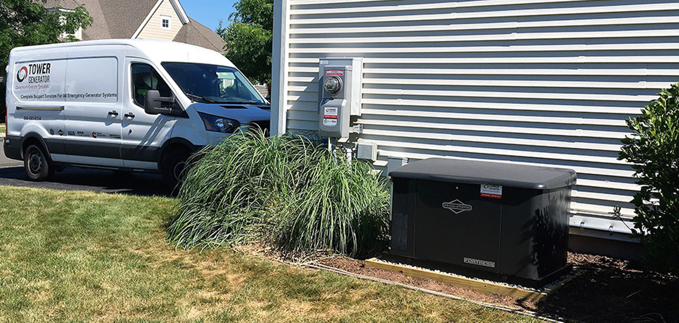 An image of residential generator outside of a house in the foreground and a Tower Generator van parked in the background