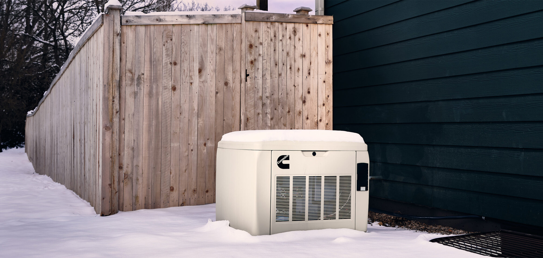 Residential generator in a yard with a layer of snow covering it.