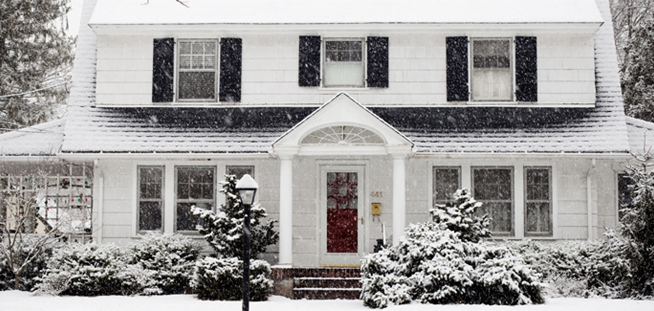 Snow falling on a white two-story residential house with black shutters.