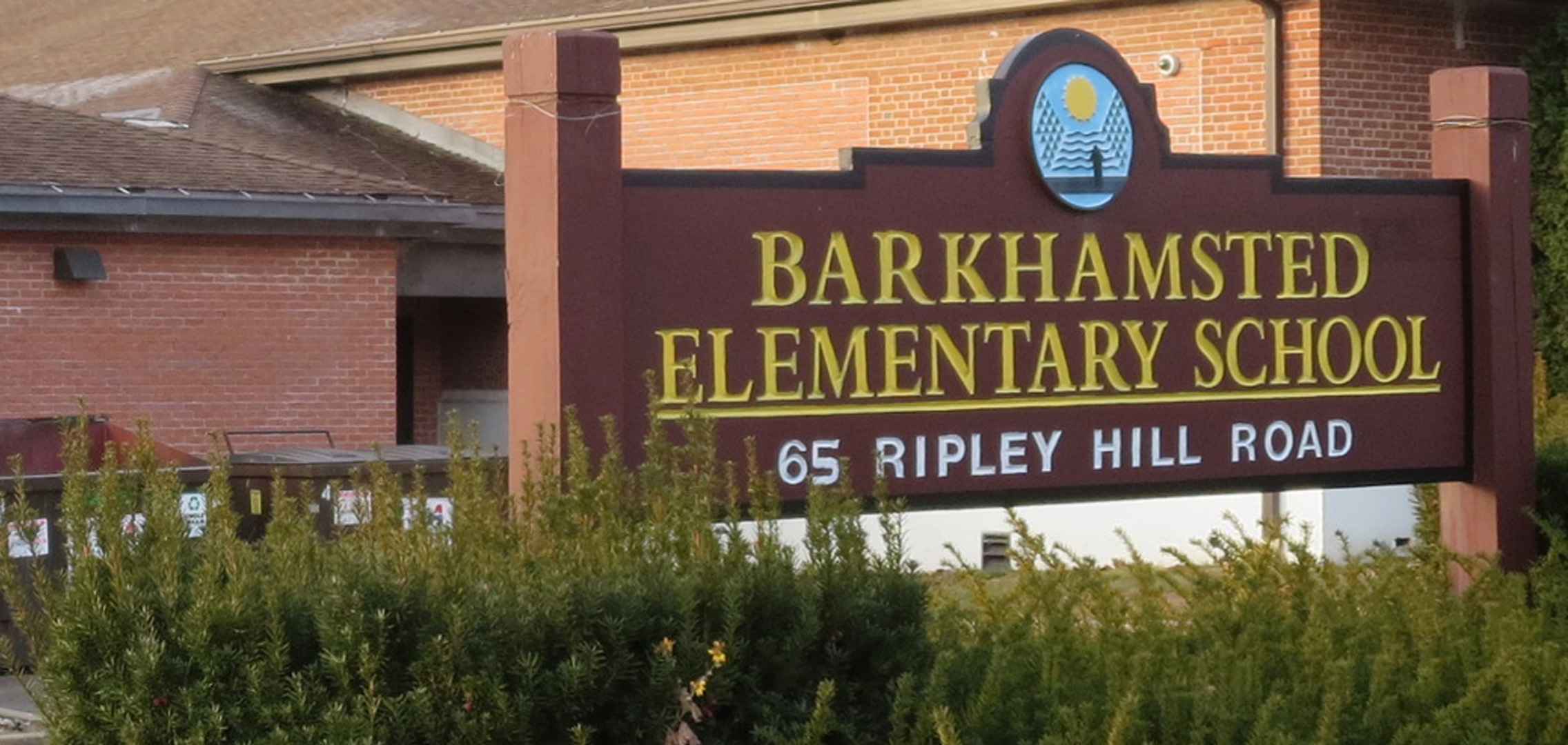 Brown wooden sign with the words Barkhamsted Elementary School in white in the foreground and a generator in the background
