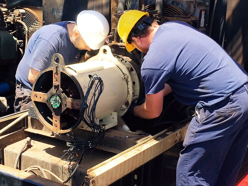 Two engineers in helmets and safety glasses working on generator