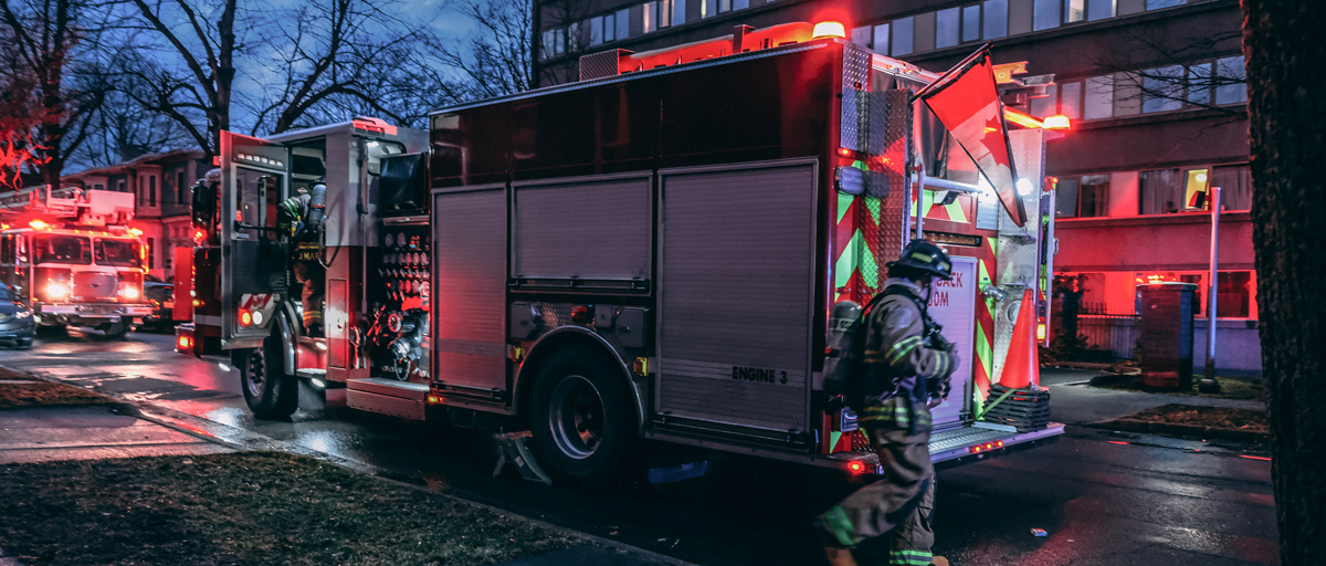 A firefighter walks past a firetruck with the lights on at night.