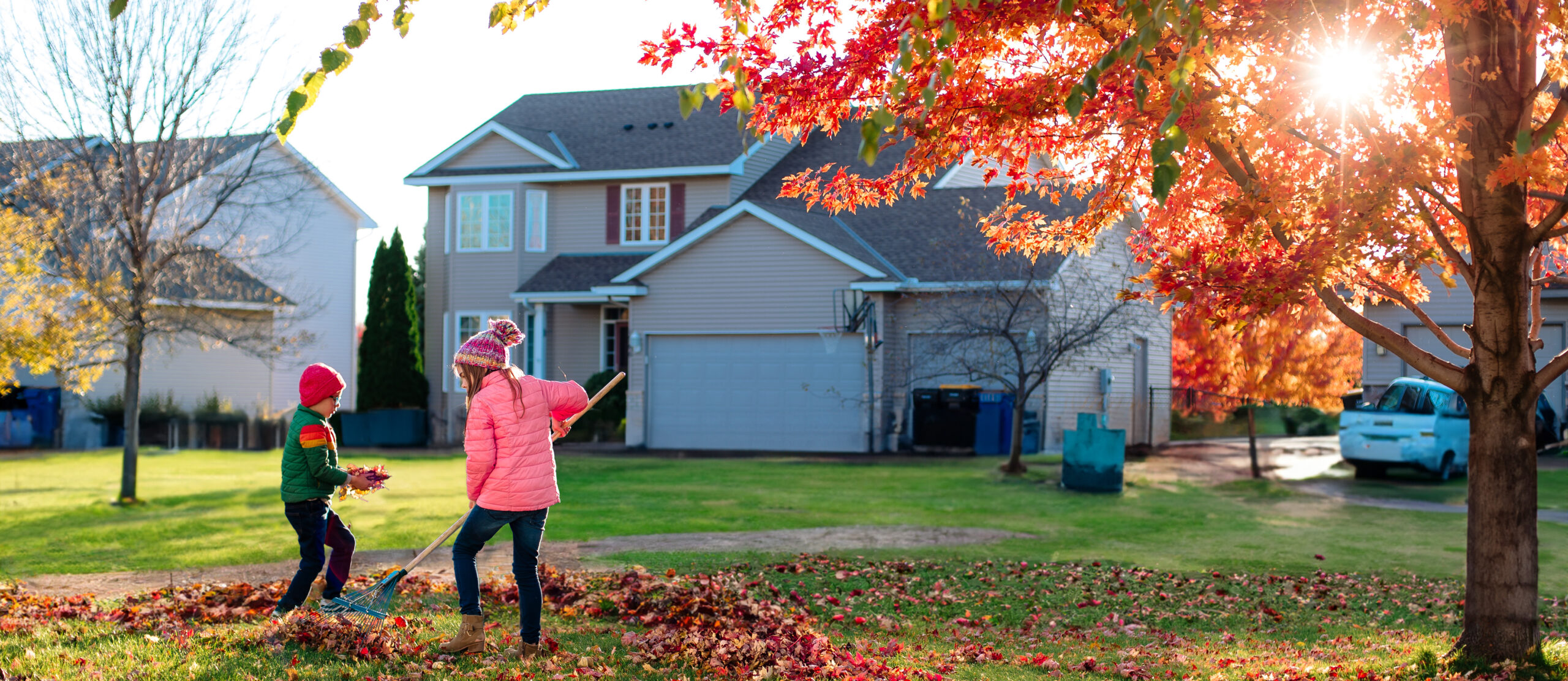 Children raking and playing in leaves in the front yard of a house.